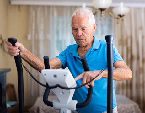 Old man using elliptic trainer at home