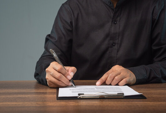 Person signing paper document on clipboard at desk