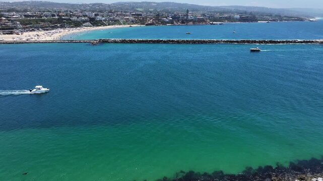 flying across Entrance Channel with boats, towards Corona del Mar State Beach, located in Corona del Mar, a seaside neighborhood in the city of Newport Beach, California where many people sunbathing