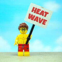 Fototapeta premium Indonesia - July 12, 2026 : Mini toy of action figure at outdoor with blur background. Miniature photography concept design. Minifigure of man male people hold 50° Celcius text at poster banner.