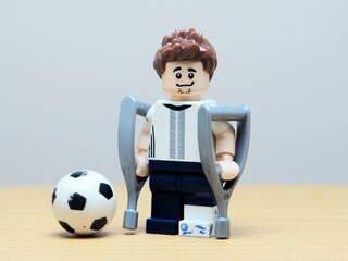 Fototapeta premium Indonesia - May 27, 2026 : Mini toy of action figure at outdoor with blur background. Miniature photography concept design. Minifigure of Injured people on crutches. Athlete character with broken leg.