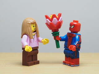 Naklejka premium Indonesia - May 27, 2026 : Mini toy of action figure at outdoor with blur background. Miniature photography concept design. Minifigure of man character give bouquet of flower to young girl. Romantic.