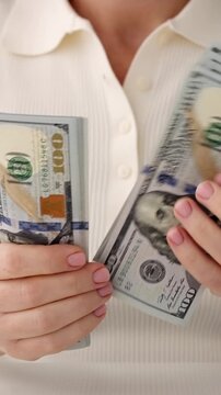 Woman hands counting hundred US dollar bills close up vertical format, female holding stack of 100 USD cash banknotes, financial business success wealth investment background