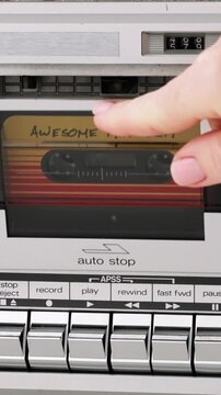 Hand inserting retro audio cassette tape into deck player vertical format, mixtape Awesome Mix Vol 1, vintage music player control buttons 80s 90s nostalgia background