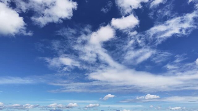 the beautiful dynamics of a bright blue sky. This video captures the movement of wispy white clouds (cirrus) and thick cumulus clouds, their shapes constantly shifting with the breeze. 