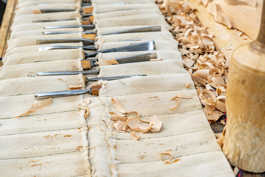 a set of wood carving chisels arranged in a canvas roll-up pouch on a wooden workbench