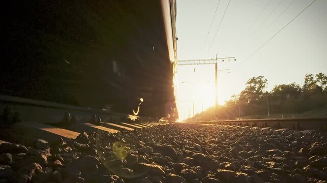 Close-up of passenger train's wheels on iron rails across sun-lit rural landscape, highlighting swift freight and passenger transportation as bright afternoon glow underscores the rail network's role