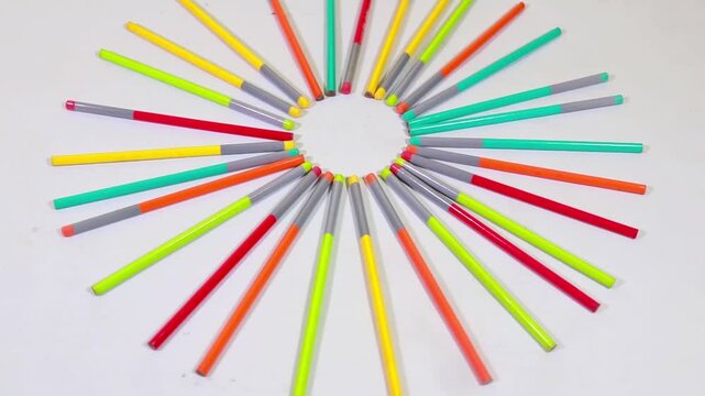 Colorful pencils arranged in a perfect circular pattern rotate slowly during this creative animation video clip on white background surface.