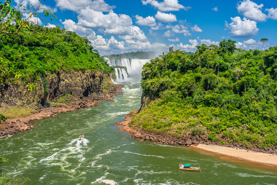 Scenic view of a powerful waterfall in the lush tropical rainforest of Brazil with tourist boats on the river