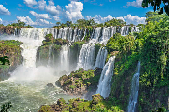 Scenic view of a massive tropical waterfall in Brazil surrounded by lush green rainforest under a blue sky with clouds