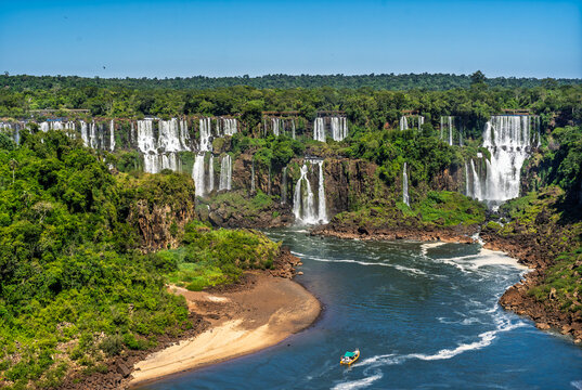 Scenic view of a large waterfall in the Brazilian rainforest with a small tourist boat on the river