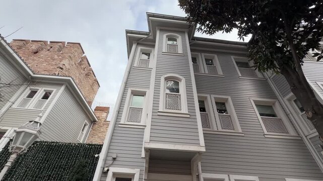 Low angle shot of a traditional Ottoman-style wooden house with ornate bay windows and lattice shutters standing beside an ancient stone wall in Istanbul, Turkey.