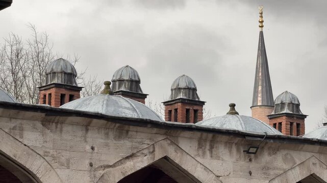 Static shot detailing the rhythmic lead domes and slender minaret of a historic Ottoman mosque against a moody overcast sky in Istanbul, Turkey.