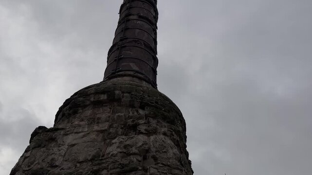 Low angle tilt up shot revealing the ancient weathered Column of Constantine standing against a dramatic cloudy sky near a historic mosque dome in Istanbul, Turkey.