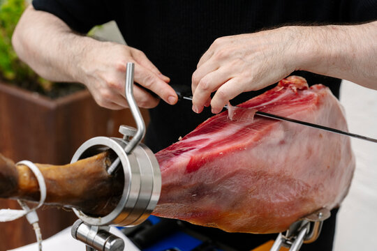 A person slicing cured ham in a realistic photo style on a neutral background, concept of culinary craftsmanship
