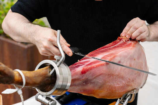Hands slicing cured ham in close-up, natural photo style, on neutral background, concept of gastronomy and craftsmanship