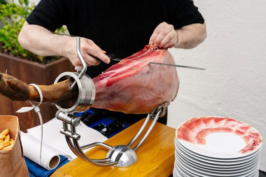 Man slicing cured ham in realistic photography style on simple background, concept of gourmet preparation and culinary craft