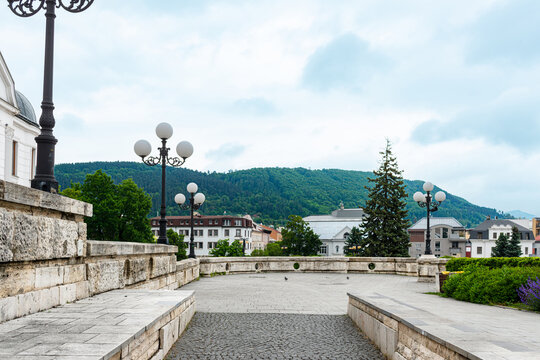 Elegant stone promenade with classic ornamental street lamps overlooking rolling forested hills and historic European architecture beneath a dramatic cloudy sky. Scenic urban viewpoint combining archi