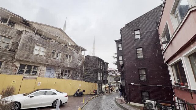 Wide angle street view of traditional wooden ottoman houses and cobblestone roads under light snowfall in the historic Sultanahmet district of Istanbul, Turkey.