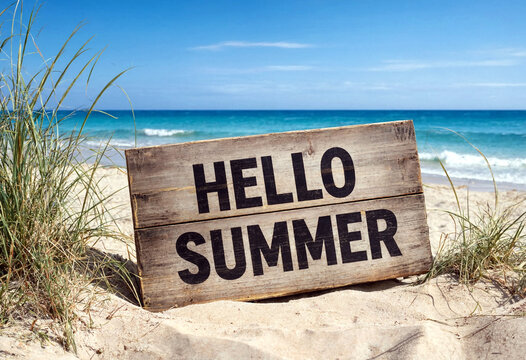 Wooden sign with hello summer text on sandy beach with ocean waves and dunes
