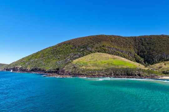 Aerial view of the clear turquoise waters surrounding Blueys Head at Blueys Beach, with the rocky headland, sandy shoreline and vibrant coastal waters along the Mid North Coast of NSW.