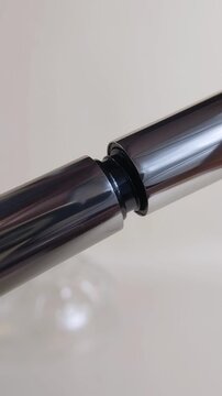 Opening the cap of silver mascara packaging. Vertical close up of beauty product for eyelashes. Makeup application tool and cosmetic container.