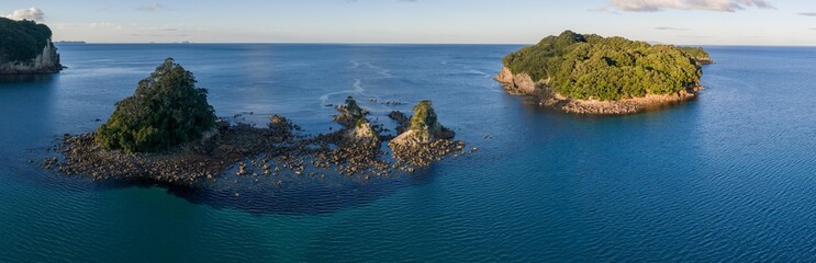 Obraz premium Scenic view of iDonut sland in the ocean near Whangamata, New Zealand.. The islands are covered in lush green trees and surrounded by deep blue water.