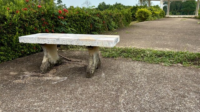 A Stone bench white color is on the strone walk way in the park.