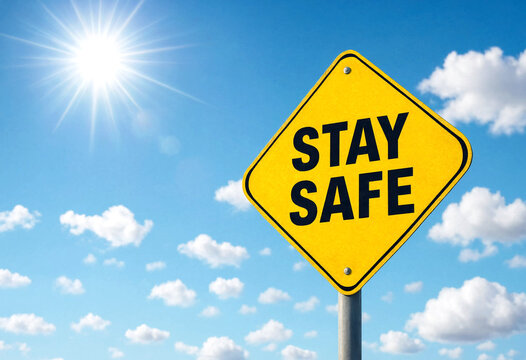 Bright yellow stay safe warning sign under sunny blue sky with clouds and sunshine
