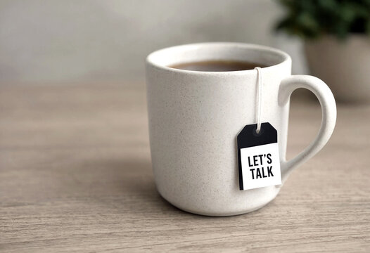 White ceramic mug with hot tea and a lets talk tea bag on a wooden tabletop surface