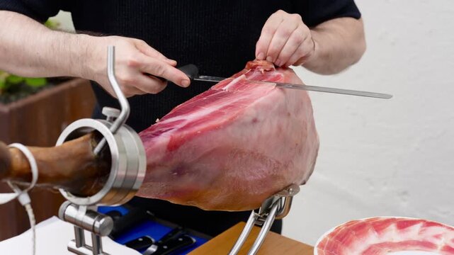 Expert ham master carving thin slices of jamon serrano from a leg held in a special stand