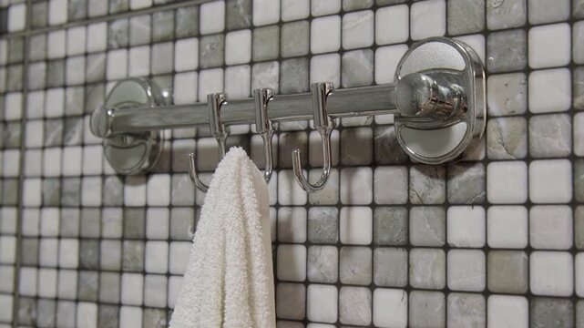 Woman hand hanging towel on hook on towel holder on wall in bathroom