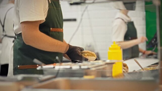 Close-up of a chef in gloves pouring sauce over the prepared filling inside a fresh pita. Concept of professionally preparing juicy and flavorful street food for takeout