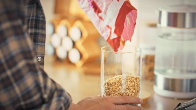 In a kitchen, a young girl's hands carefully pour oatmeal into a storage jar, promoting healthy eating through organized food storage, reflecting a thoughtful approach to nutrition