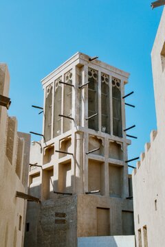 Traditional Arabian wind tower barjeel against blue sky in a historic old town district with sandy plaster walls