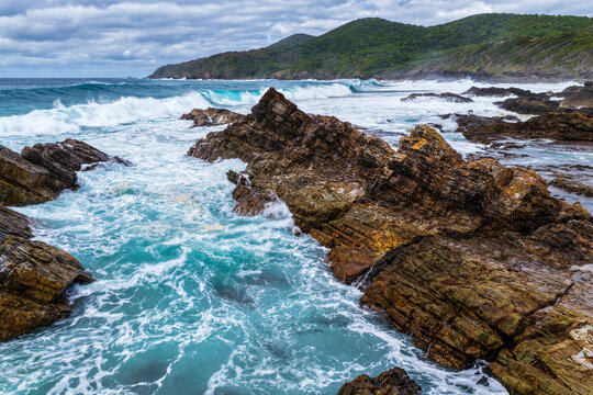 Aerial view of powerful waves breaking across rugged rock formations, creating swirling whitewash along the coastline at Burgess Beach, Forster on the Mid North Coast of NSW