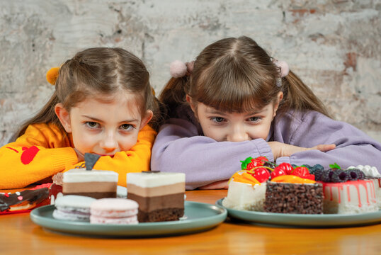 Two girls enjoy desserts while resting on a table made of wood in a simple indoor setting during the afternoon