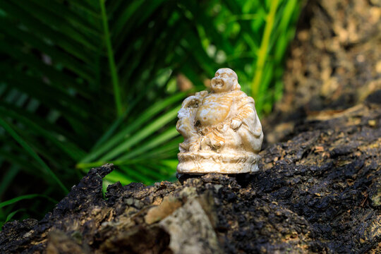 A small figurine of the Japanese god of fortune, Hotei on stone against natural background. Hotei symbolizes happiness and carefree living. Miniature sculptures known as netsuke or okimono