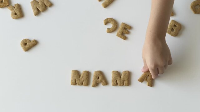 Alphabet biscuits scattered on a table become a fun learning tool as a childs hands form simple words Mama. Clip captures education, parenting, family lifestyle, and the joy of playful childhood