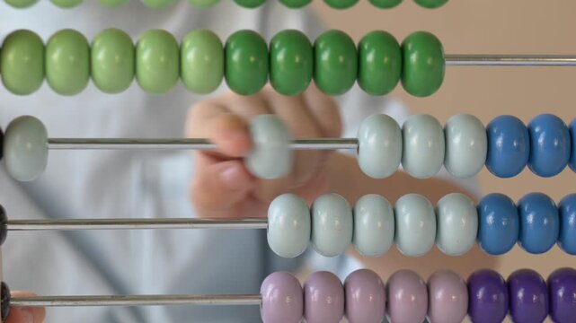 Finger of a young child pushes vibrant yellow beads across an abacus rod in close detail. The intimate shot highlights focus, early cognitive development, and joyful discovery in a cheerful setting.