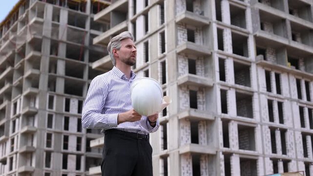Tired male engineer taking off safety helmet touching forehead while working at construction site
