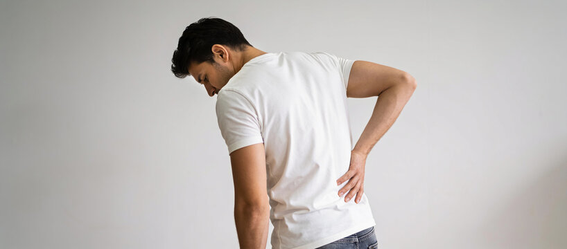 Man bending forward while holding his lower back with both hands, representing physical discomfort and back pain