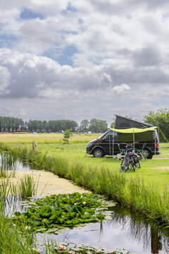 Family campervan parked by a pond with bicycles and a green awning on a cloudy summer day in Friesland, The Netehrlands