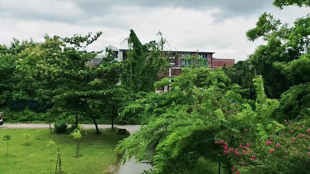 Lush green trees and dense foliage framing a modern red brick multistory building under a cloudy sky in a rural park