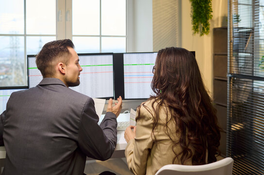 Colleagues man and woman discussion spreadsheets screens. They review data on triple screens in office, debate figures, and check entries for accuracy. Teamwork guides clear financial decisions.
