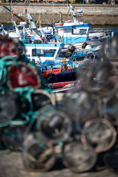 Traditional Stacked Fishing Traps on the Pier of a Galician Harbor with Trawlers Docked in Northern Spain