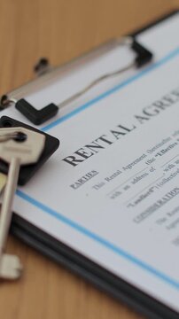 Vertical video Close-up view of a rental agreement document with key, and a pen placed on top. Property rental, leasing contracts, real estate.