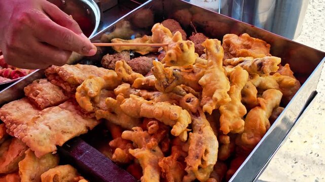 Traditional Indonesian fried snacks displayed at a street food stall while a vendor selects fresh fritters for customers. Authentic local cuisine featuring crispy homemade snacks and vibrant street fo