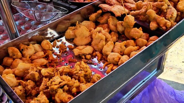 Traditional Indonesian fried snacks displayed at a street food stall while a vendor selects fresh fritters for customers. Authentic local cuisine featuring crispy homemade snacks and vibrant street fo