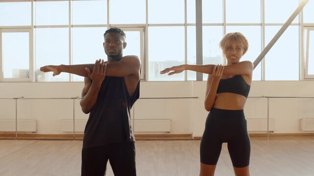 African Fitness Young Couple performs partner arm stretches in a bright fitness studio, preparing for a workout. Casual activewear, natural light and focused expressions convey health lifstyle 4k